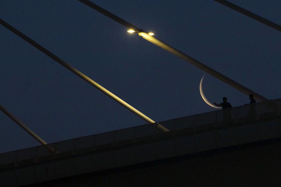 A view of a crescent moon behind a bridge structure.