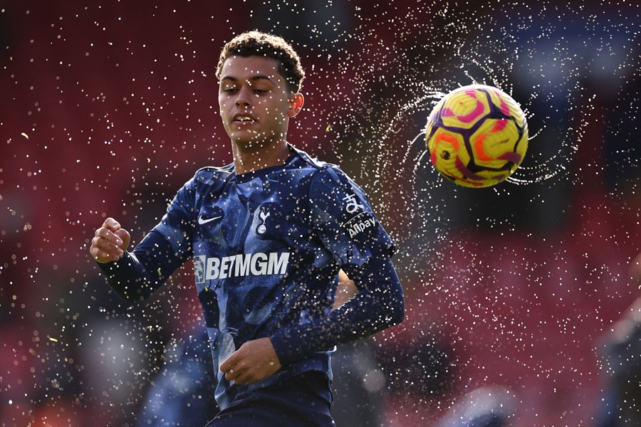 A soccer player warms up for a game, as a wet ball spins in the air nearby, throwing off curving streams of water.
