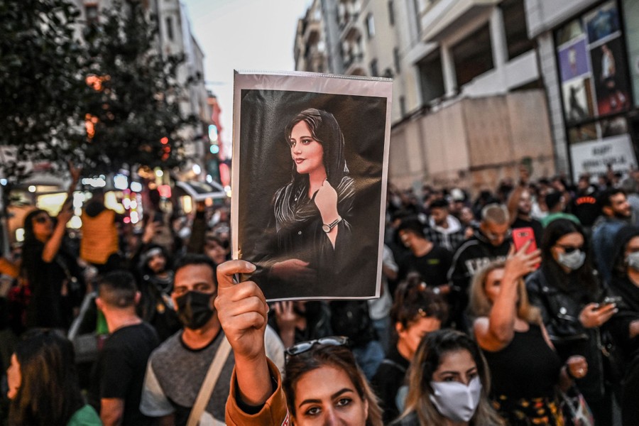 Protesters march down a street, with one at the center holding up a portrait of a young woman.