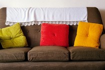 A brown couch with three throw pillows—one green, one red, one yellow—and a white blanket on the back