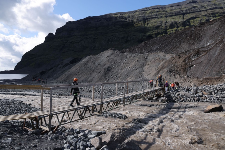A group of visitors walks across a makeshift bridge over a small river.