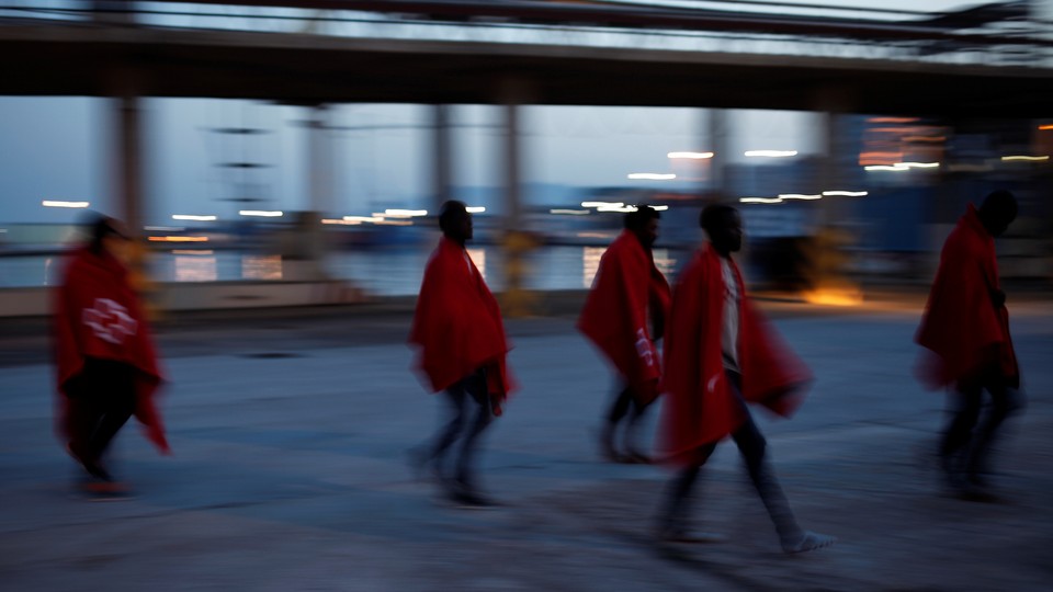 Five young migrants wearing Red Cross blankets walk in the Port of Malaga.