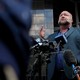 A photo of Alex Jones standing before microphones at a press conference outside a Houston courthouse