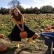 A child smiles while lifting a heavy pumpkin by its stem in a pumpkin patch.