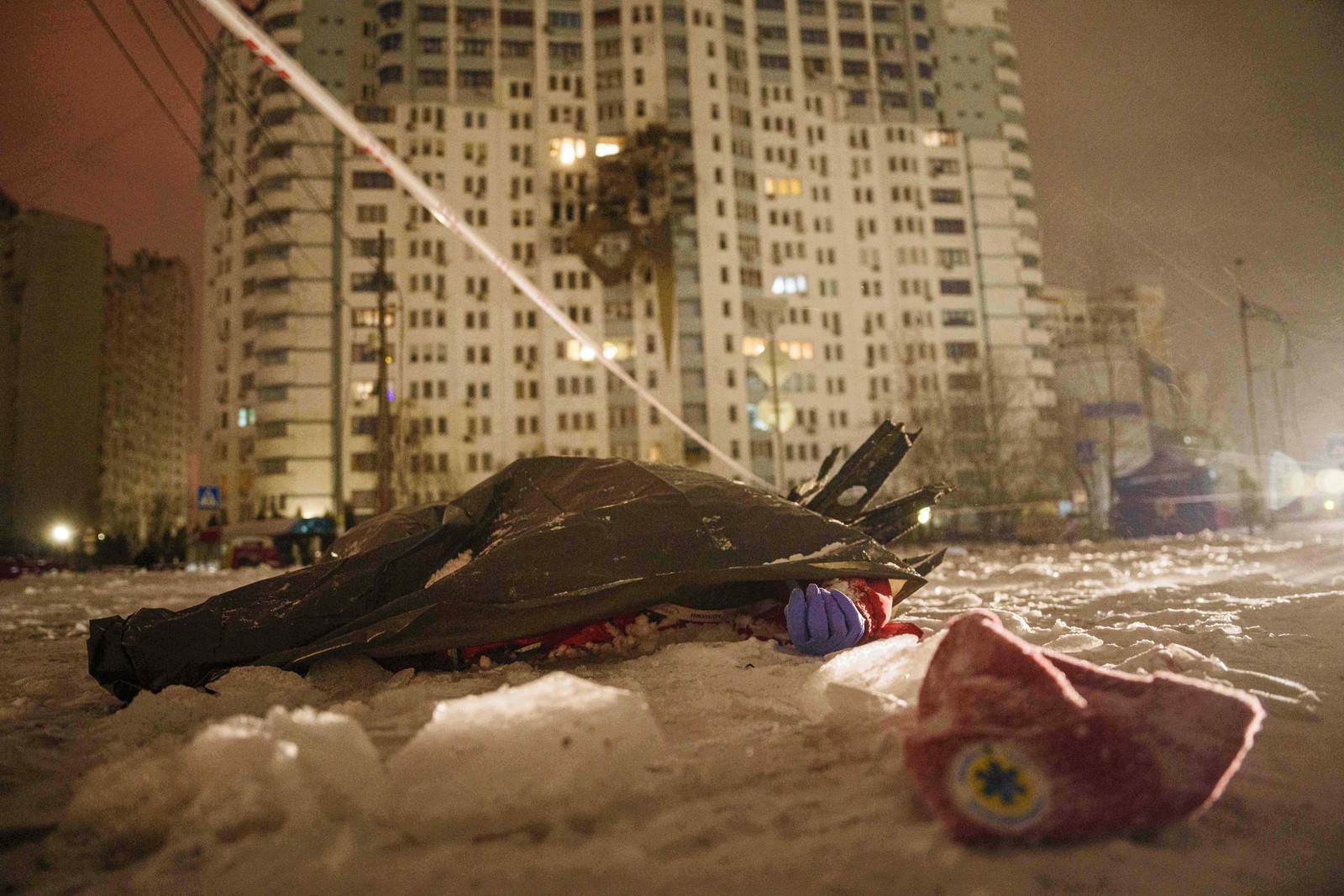 A body, covered with a tarp, lies on the ground outside a bomb-damaged apartment building.