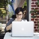 A young man looks thoughtfully at a laptop while sitting at a cafe