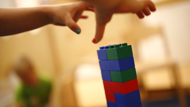 Two children's hands grab for a tower of LEGOs.