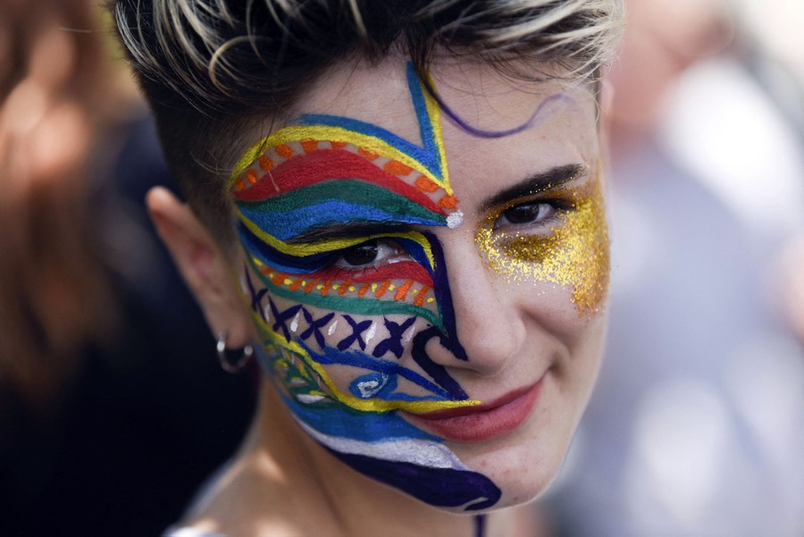 A person with colorful makeup on their face takes part in a march.
