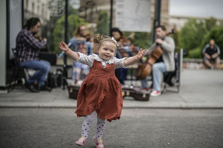 A young girl dances near a string quartet playing at a bus stop.