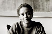A black-and-white photo shows the poet Nikki Giovanni sitting at a table.