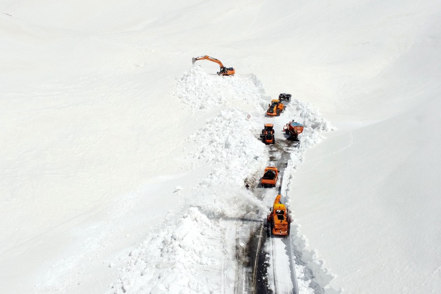 An aerial view of several pieces of construction equipment being used to clear deep snow from a mountain highway