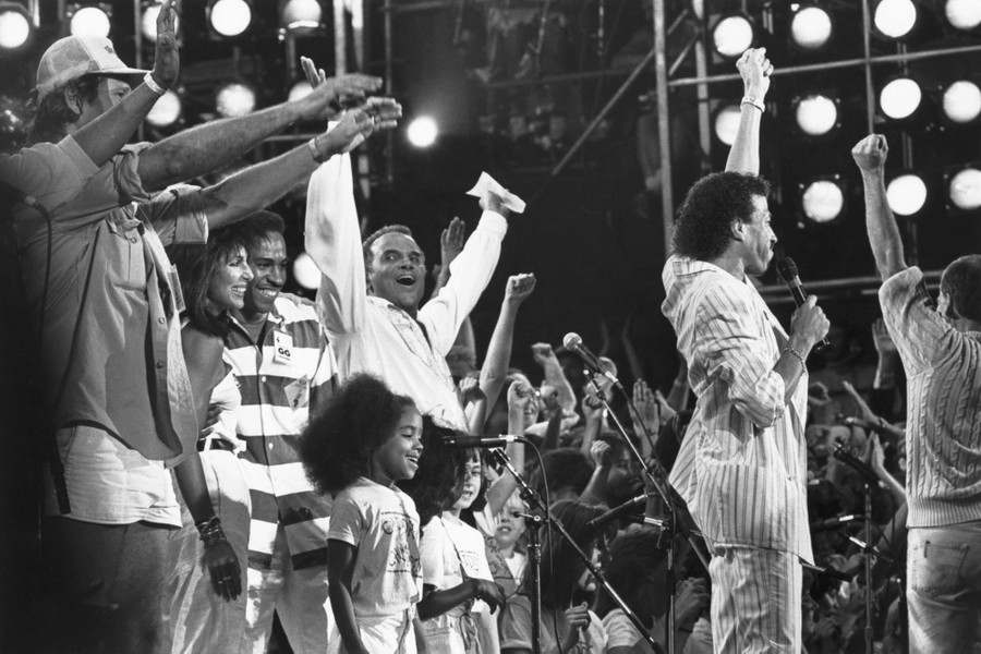 A group of performers raise their arms, celebrating onstage.