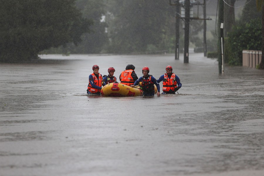 Several rescue workers walk in waist-deep water, pulling a person along in an inflatable raft.