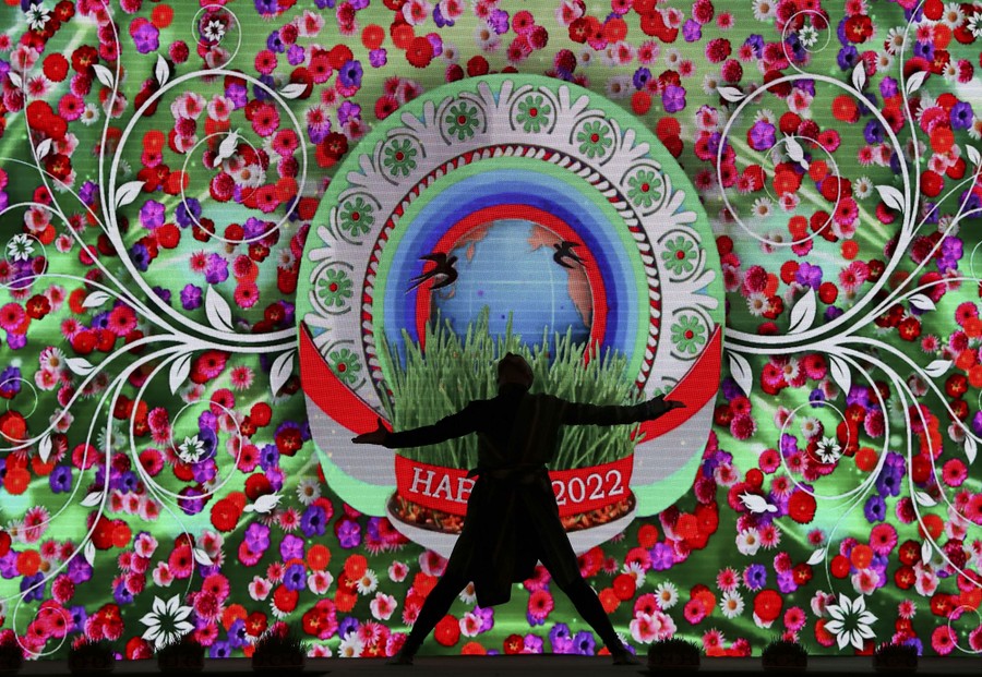 A person performs, silhouetted on a stage in front of a colorful background.