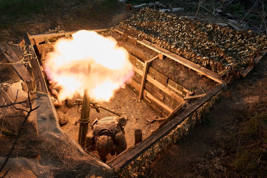 A soldier kneels down inside a ditch while firing a mortar as flames erupt during the launch.