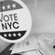 A black-and-white photograph of ballots and a Vote NYC sticker