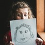 A little girl holds up a picture of herself that she has drawn.