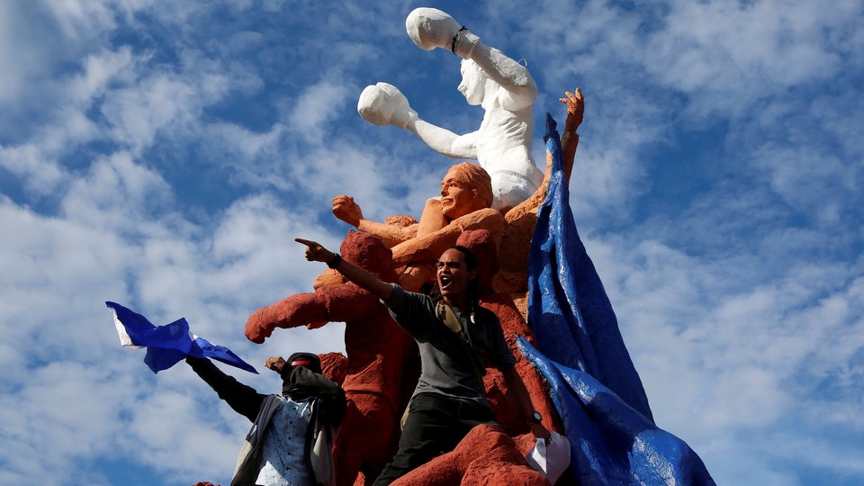 Protestors hold Nicaraguan flags standing on a statue