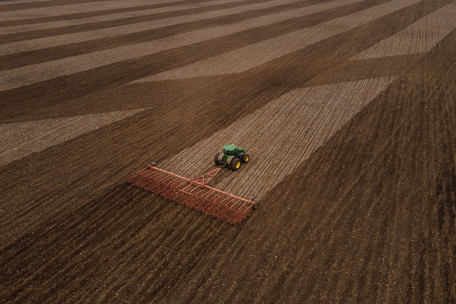An aerial view of a tractor pulling a rig, tilling soil in a large field