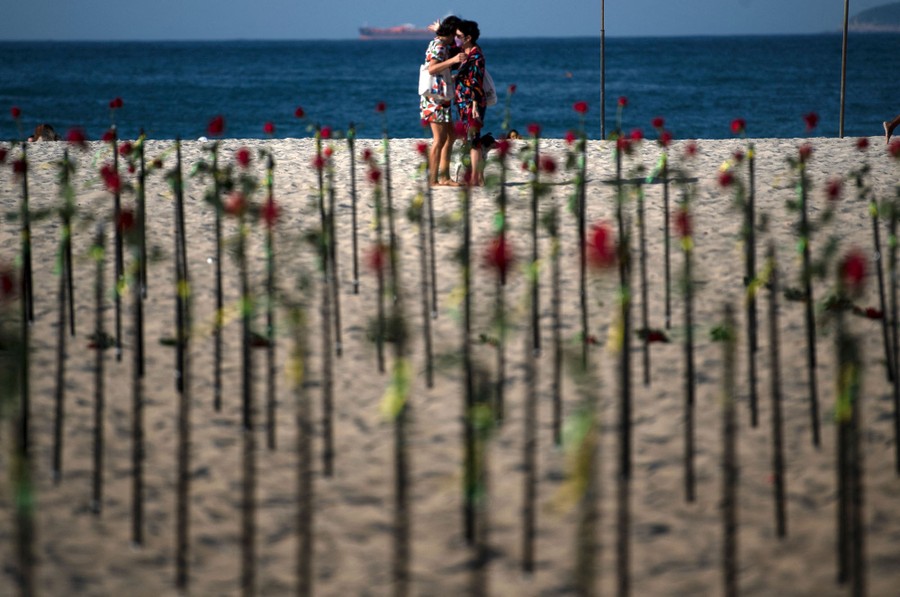 Two people embrace on a beach near a memorial made of roses.