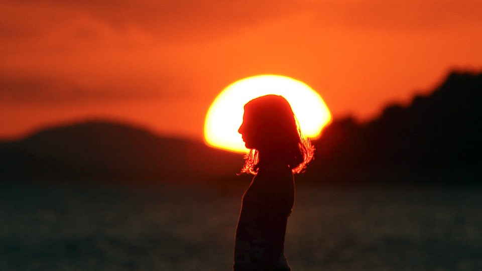 A girl stands in front of a setting sun