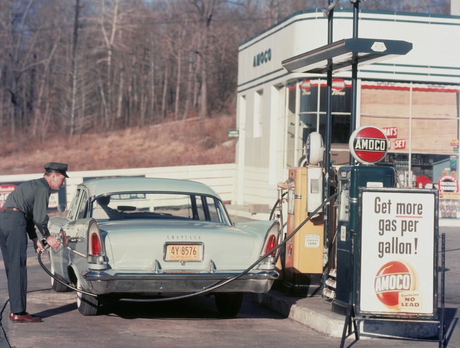 A man working at a gas station fills up a vintage Chrysler