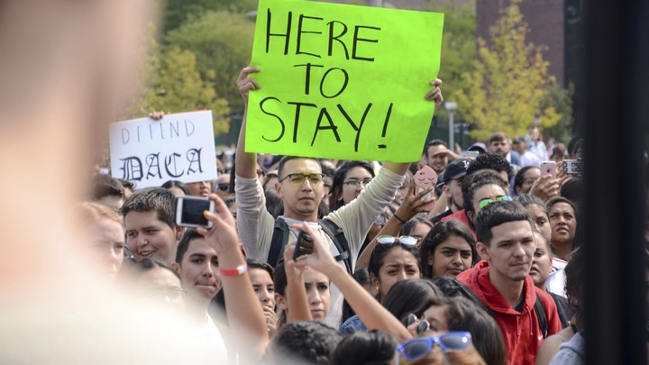 A protester holds a sign that reads "Here to Stay!" 