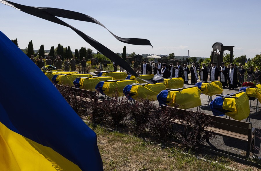 People gather outside, around 13 coffins draped in yellow-and-blue flags.