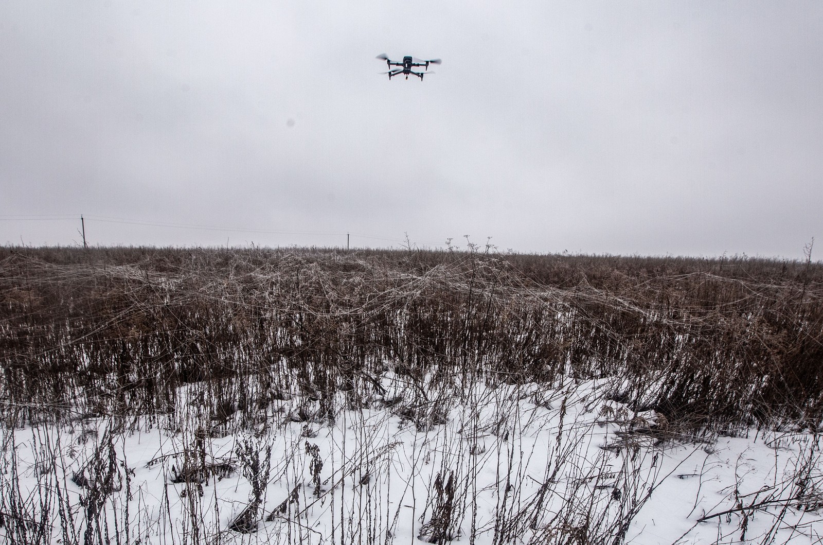 A small reconnaissance drone flies above a field covered by discarded fiber-optic drone fibers.
