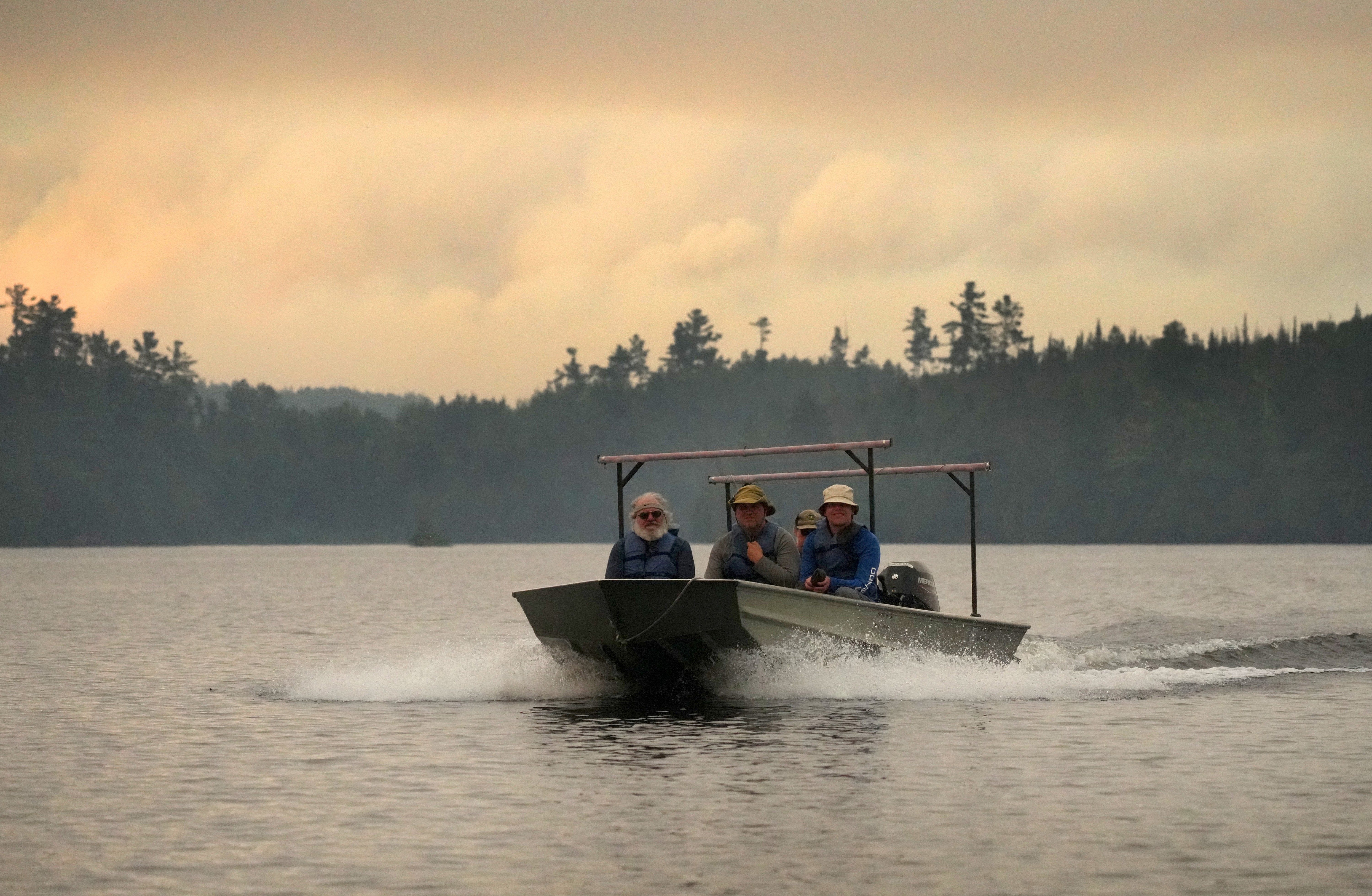Several people in a small boat motor across a lake beneath smoky skies.