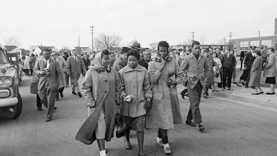 The black and white photos features four black students walking together as white students look on.