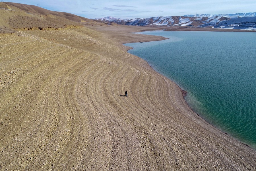 A person walks on a striped slope toward the shoreline of a reservoir.