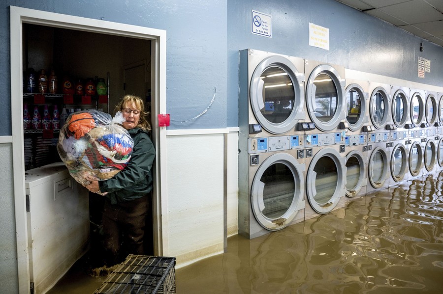 A person carries a bag of clothing inside a flooded laundromat.