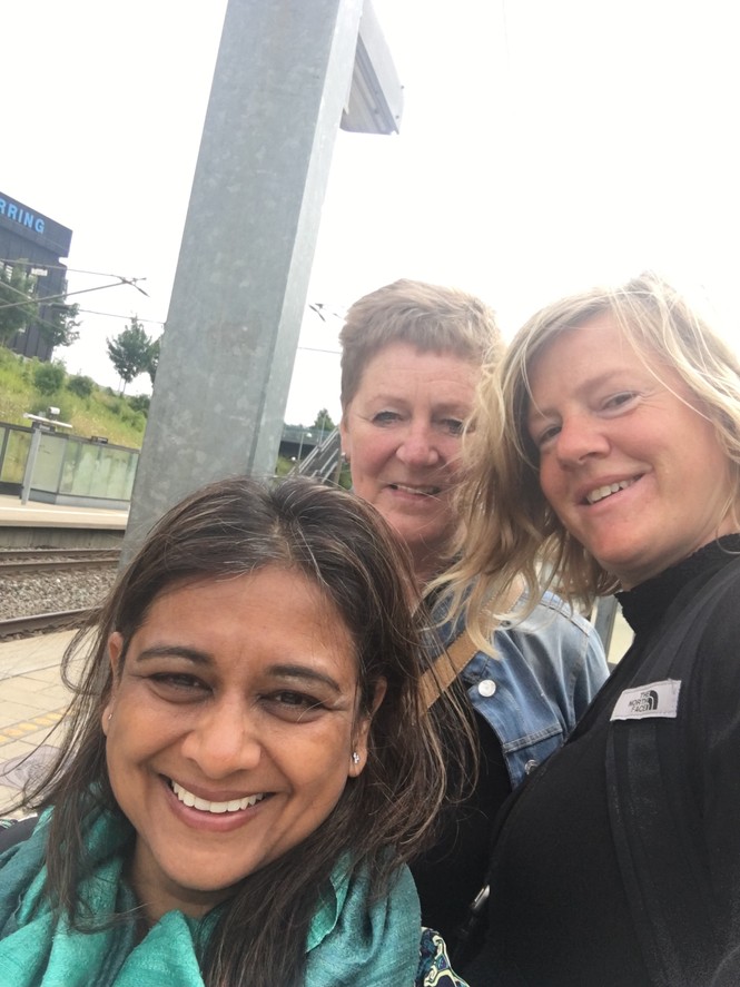 Three women smile for the camera on a bright sunny day, their hair appears mussed by the wind.