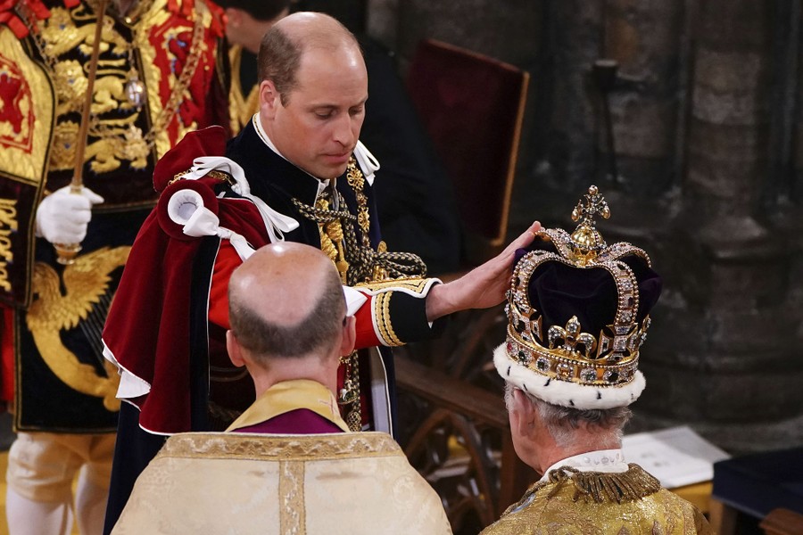 Prince William reaches out to touch the crown atop his father's head.