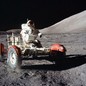 An astronaut drives a lunar rover toward the photographer, on the surface of the moon.
