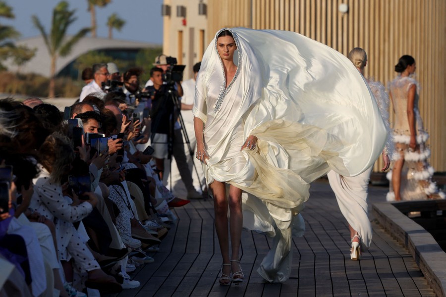 A model walks on an outdoor runway, their garment billowing in the wind.
