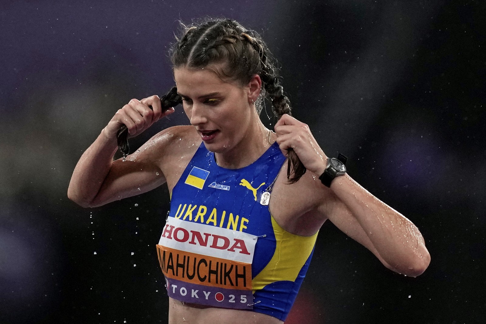 An athlete wrings water from their pigtails after competing in heavy rain.