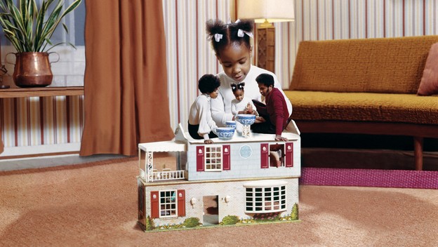 A young child plays with a doll version of her family in a dollhouse