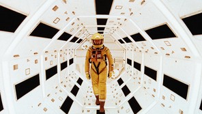 A man in a yellow spacesuit stands in a futuristic white tunnel in a scene from "2001: A Space Odyssey"