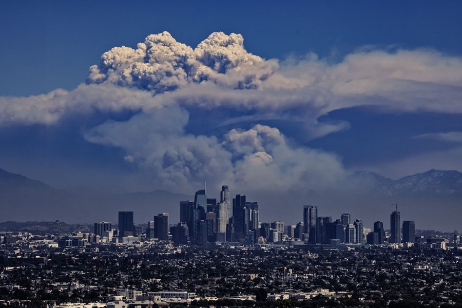 A huge cloud of smoke rises above mountains, seen in the distance behind the Los Angeles skyline.