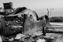 A black and white photograph of a man looking at a burned down home