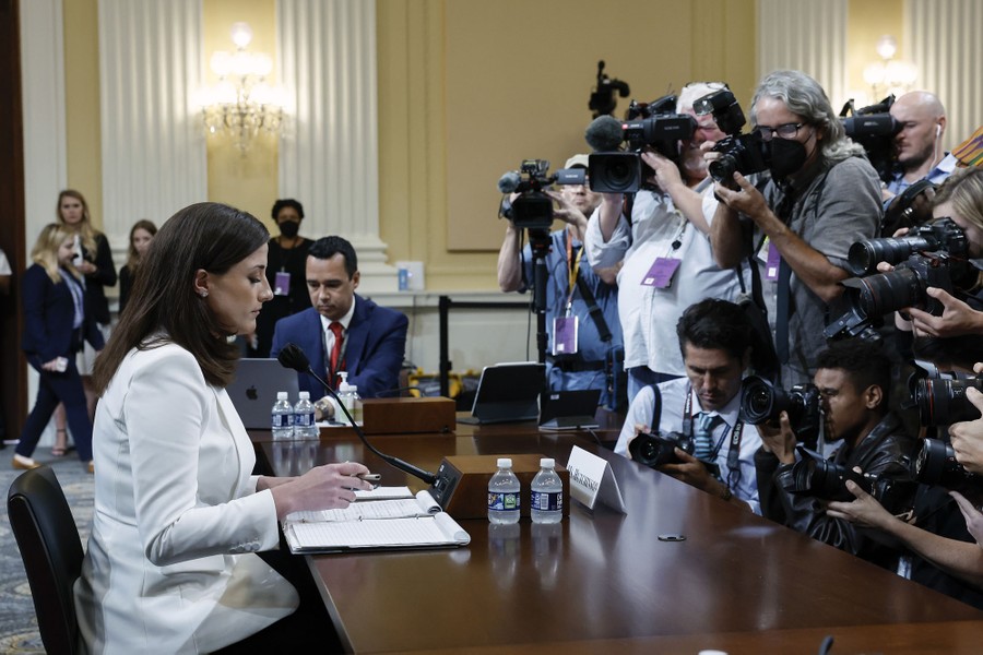 Many press photographers crowd together to photograph a woman seated at a table.