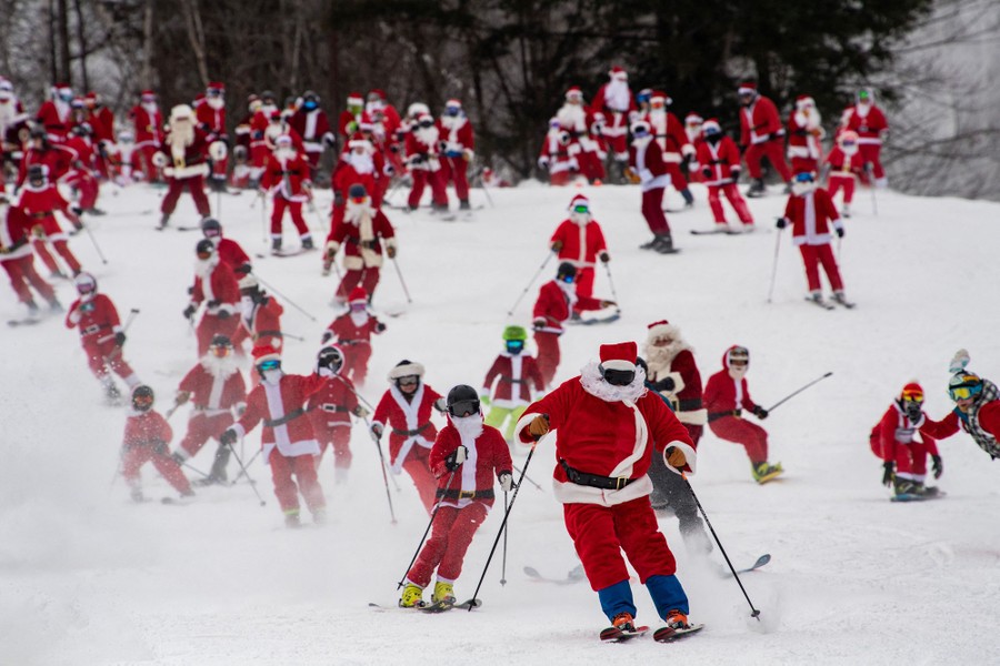 Dozens of people dressed as Santa Claus ski down a hill.