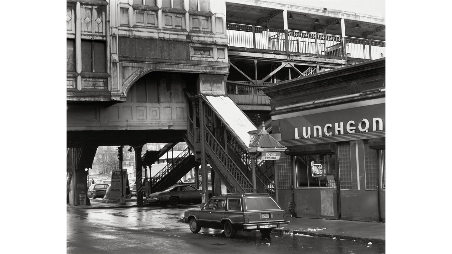 black-and-white photo of Boston's Washington Street Elevated in the 1980s with Dover station exit, diner with "Luncheon" neon sign, wood-paneled station wagon