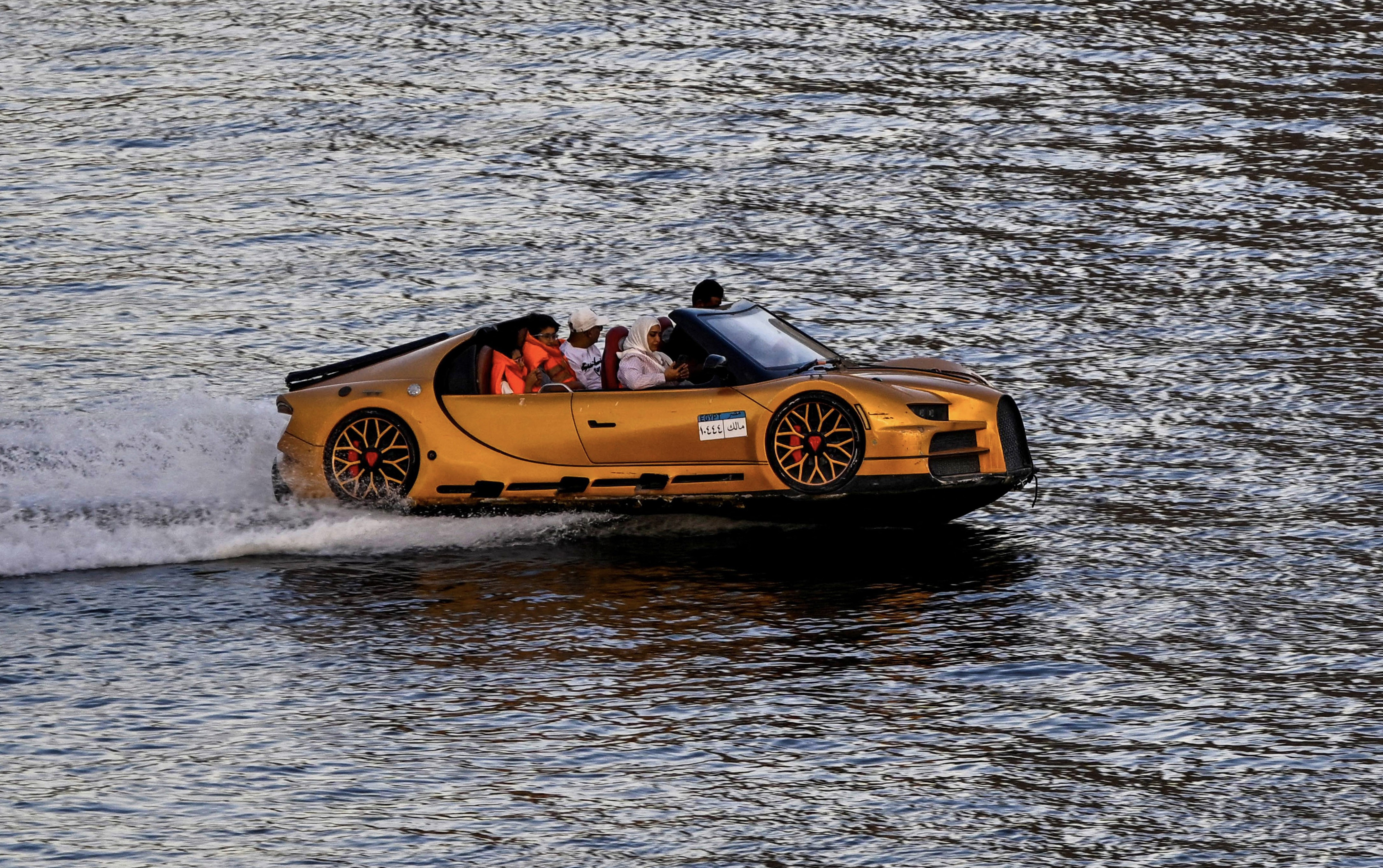 A car-shaped river taxi carries passengers down a river.