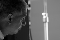 A black-and-white photo of Errol Morris in profile peering around a screen