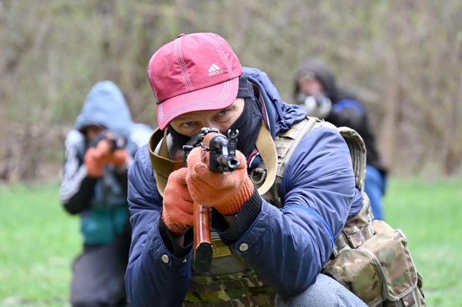 Several people train in a field, carrying weapons.