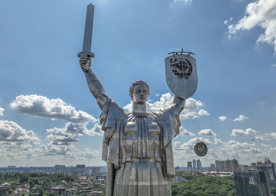 Workers remove the coat of arms of the former Soviet Union from the shield of a tall metal statue.