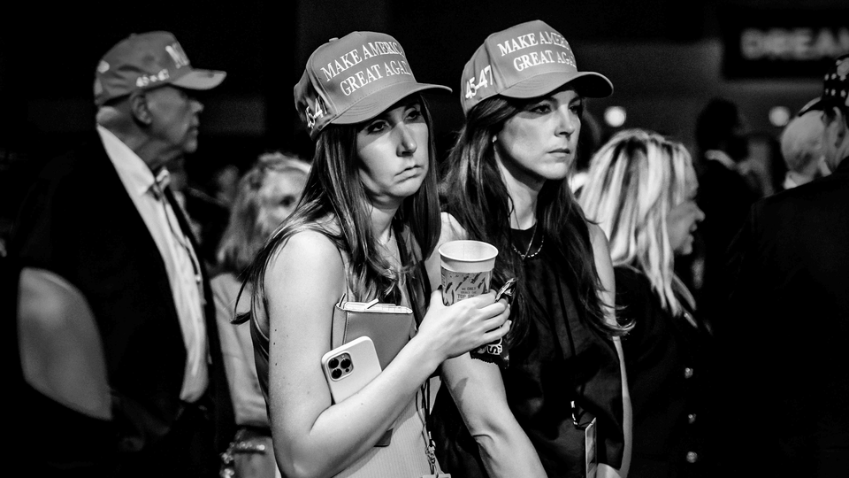 Black-and-white photograph of two women wearing MAGA caps frowning